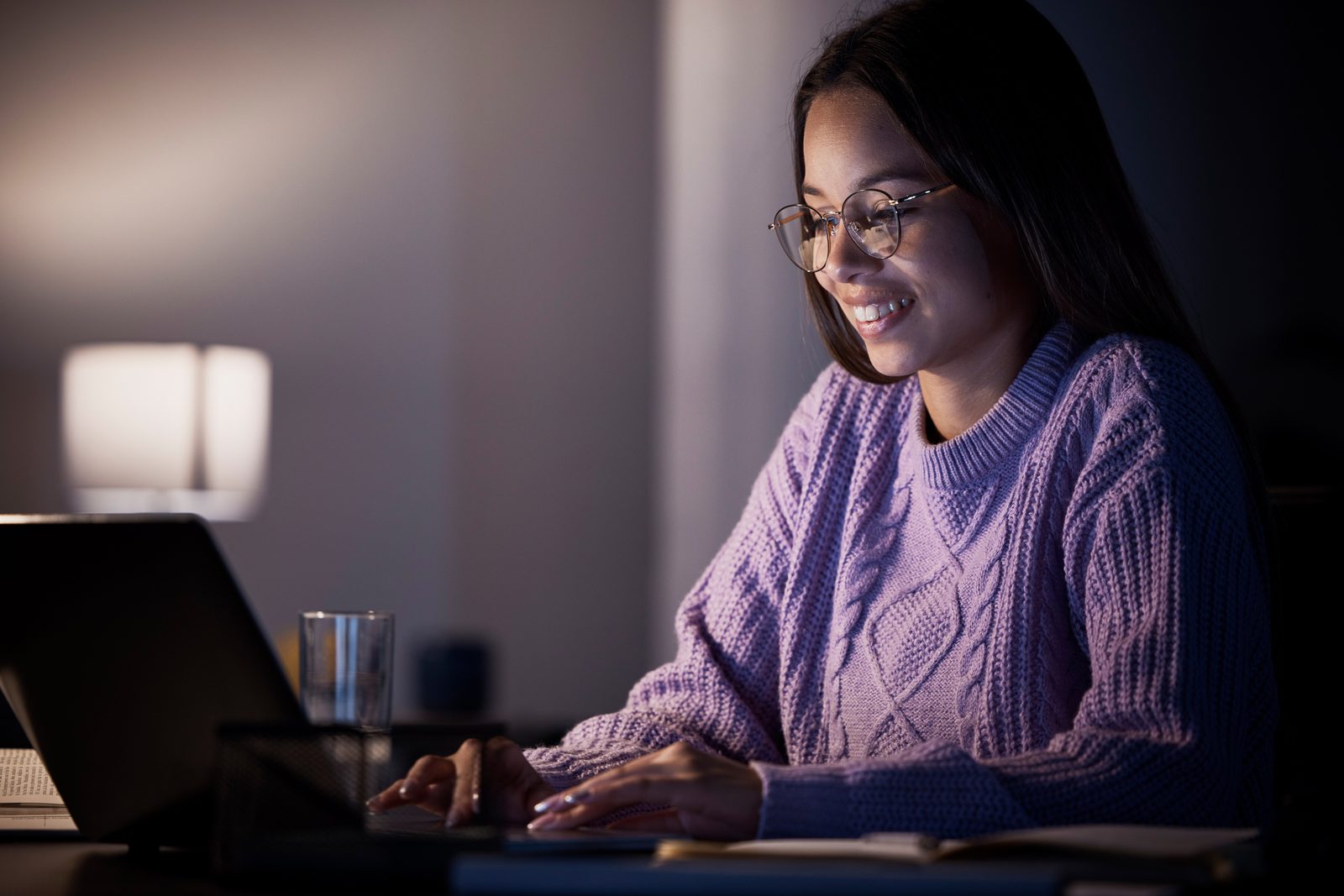 Aluna estudando EAD à noite em casa, sorrindo, com o notebook